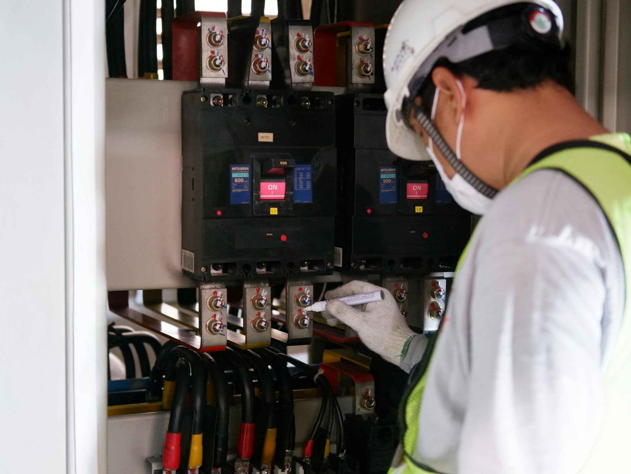 Technician wearing safety gear inspecting electrical panels in an industrial setting.