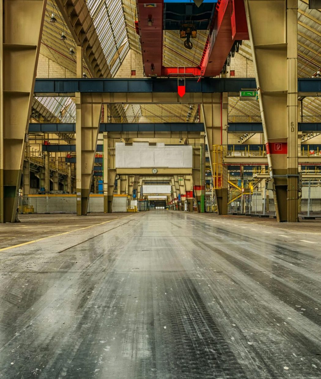 Wide view of an empty industrial warehouse with visible cranes and metal structures.